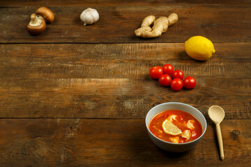 Tom yum soup with chicken in a plate on a wooden table. Copy space.