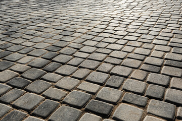 The surface is paved with road tiles of different sizes (multi format). The uneven (melange) color of the tile makes it look like a natural stone. Perspective viewpoint.