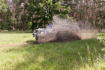 A military all-terrain vehicle travels through the countryside through puddles of mud.