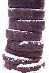 A column of old black car tires under white snow. Car tires are stacked vertically on top of each other on a white background. Isolated photo of the wheels. copy space