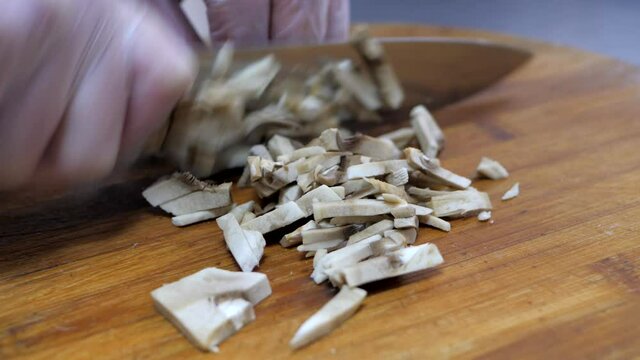 Chef in gloves cuts mushrooms on the wooden cutting board, preparing ingridients for appetizing dish. 