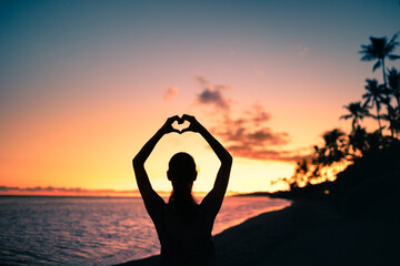 silhouette of a woman on the beach making heart shape with hands.  Love, and peace in nature concept. 