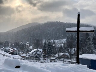 a cross on top, against the background of a village in the forest covered with snow