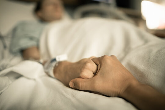 Person giving sick loved one support. Man holding woman's hand lying in hospital bed. 