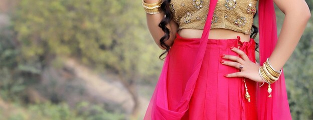 Waist of a woman with golden and pink sari, jewelries and red nails