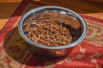 Dry dog food in a metal bowl on a carpeted floor.