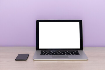 open laptop with and smartphone on a wooden table against a lilac wall