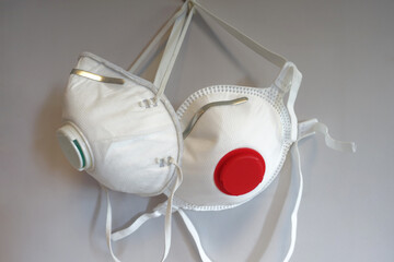 Two anti-virus face masks with filters hanging on grey wall close up. Two white breathing reusable...
