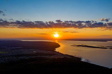 The setting sun over a wide, deep, flat river. There is a summer cottage village on the river Bank. Shooting from a drone. Copy space.