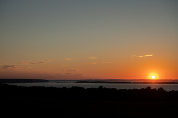 Summer landscape. Red sunset over a wide flat river with wooded banks. Copy space.