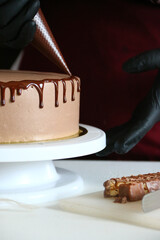 liquid chocolate on cake. A confectioner squeezes liquid chocolate from a pastry bag on to a cream biscuit cake with background