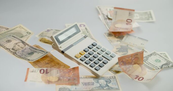 Calculator and falling paper currency. View of an old calculator and international paper currency. Counted summ on calculators screen. Money signs. Counting money. Home finances concept.