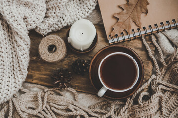 Sweaters and cup of tea with notebook, candle and knitting clothes. Cozy autumn or winter concept.