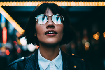 Youthful female traveller in stylish spectacles for vision correction spending time for walking around metropolitan downtown and explore New York nightlife on leisure, young woman in streetwear