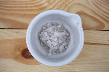 Large white crystals of potassium nitrate in a ceramic mortar, on a wooden table.