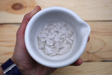 Ceramic mortar with large white crystals of potassium nitrate in a male hand.