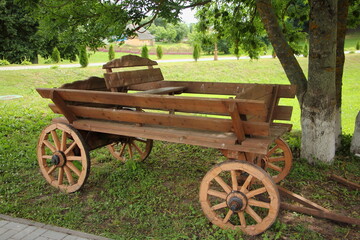 Fototapeta na wymiar Russian rustic retro transport - empty vintage style horse cart on wooden spoked wheels in the Park Garden on green grass background on a summer day