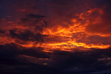 Fototapeta premium Heavy black orange colorful dramatic stormy clouds on sunset with sun rays lighted sky on a summer evening, beautiful cloudscape view, texture for background and wallpaper