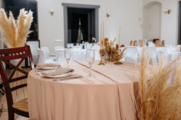 Romantic table setting in a restaurant for a holiday. Wedding decor for newlyweds at a banquet. Dried flowers floristry and candles, boho style. Cartering service for the bride and groom and guests.