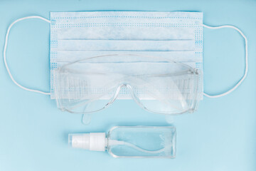 Hand sanitizer, medical mask and protective glasses on blue background.