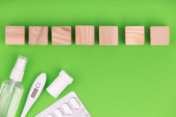Pills with sanitizer and thermometer on green background.