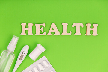 Pills with sanitizer and thermometer on green background. Word health made of wooden letters.
