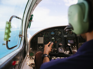 Over the shoulder of pilot flying a small plane over the ocean water with view of the cockpit - obrazy, fototapety, plakaty