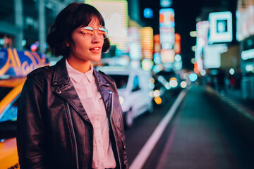 Trendy dressed hipster girl in eyewear with night city light reflection fascinated with beautiful...