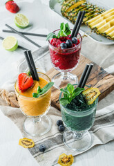 Variety of fresh tropical smoothies with kiwi, mint, blueberries, strawberry, mango in jars glass on light background. Summer cold drink and cocktail