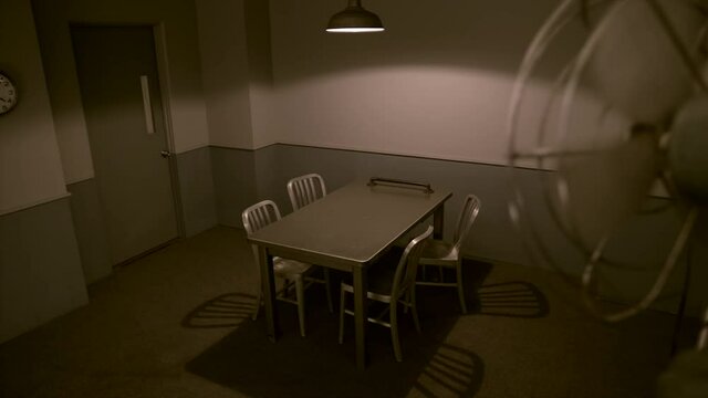 HIGH ANGLE, EMPTY INTERROGATION ROOM SHOT.  SLOW SLIDER, FROM BEHIND A FAN.   IN 4K, 10 BIT, 4:2:2.  NO PEOPLE.