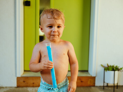 Young boy toddler eating blue popsicle on back porch of modern home in the summer