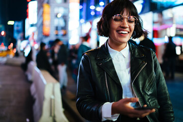 Cheerful stylish brunette hipster girl with short haircut laughing while walking with phone on...