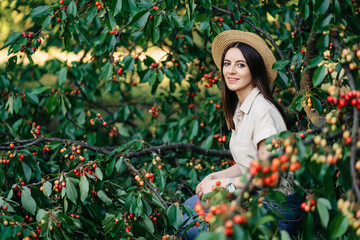 Portrait of a young cheerful woman in a straw hat with a basket cherries