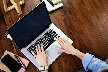 Mockup image of a woman using laptop with blank screen on wooden table