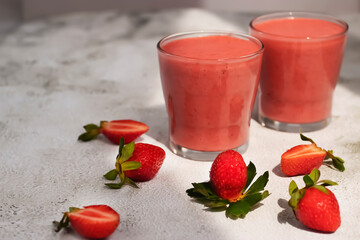 Organic strawberry smoothies in glass cups and ripe strawberries on a gray cement background.