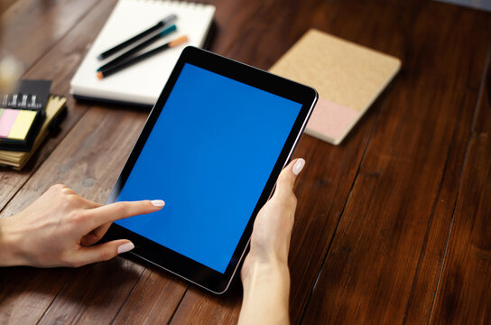 Mockup image of a woman using digital tablet with blank screen on wooden table. Close up photo of female hands holding device vertically