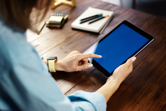 Mockup image of a woman using digital tablet with blank screen on wooden table. Close up photo of female hands holding device vertically