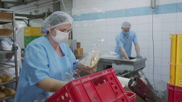 An employee working in a bakery. The baker spreads the sliced bread on an automatic packaging machine at the factory