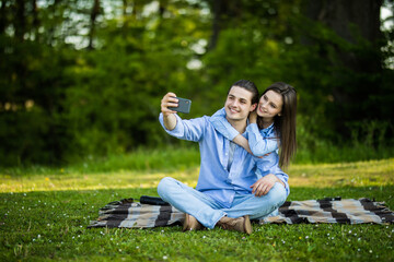 Lovely couple have fun together, sit on plaid outdoor, enjoy sunny warm weather, pose for making selfie at camera