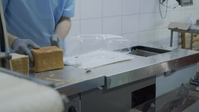 Bakery worker packs sliced bread in plastic bags. Production and packaging of bread.