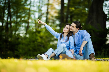 Holidays, vacation, love and friendship concept. Smiling couple sitting on grass and pointing finger in park