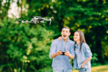 Portrait of man and woman is operating the drone by remote control in the green park. Man and woman is playing with quadrocopter outdoors.
