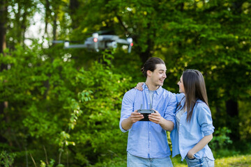 Naklejka na ściany i meble Portrait of man and woman is operating the drone by remote control in the green park. Man and woman is playing with quadrocopter outdoors.