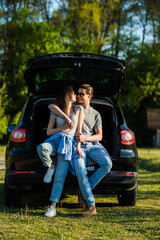 Naklejka premium Happy young couple sitting in trunk of their new car in countryside