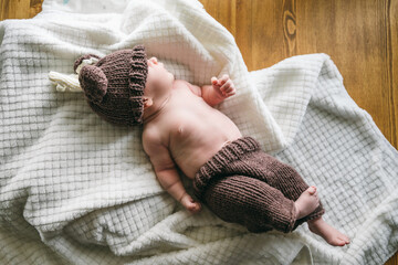 Newborn baby two-months-old smiles and lies on a white blanket in a knitted deer costume for newborn photography. Psychomotor development and baby care