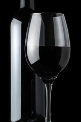 Detail of a glass of red wine next to a bottle on a black background