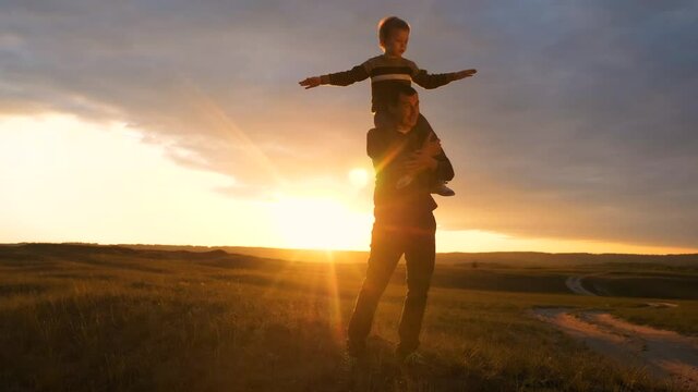 happy family. son sits on his neck teamwork at father shows hands to the side plays at the pilot depicts an airplane silhouette at sunset. happy family concept childhood man dad with little boy