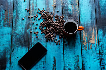 filtered morning coffee in an orange cup and coffee beans with smartphone on blue wooden table