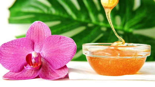 4k. sugar paste or wax honey for hair removing flows down from wooden waxing spatula sticks - depilation and beauty.