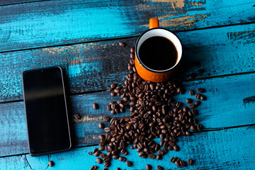 filtered morning coffee in an orange cup and coffee beans with smartphone on blue wooden table